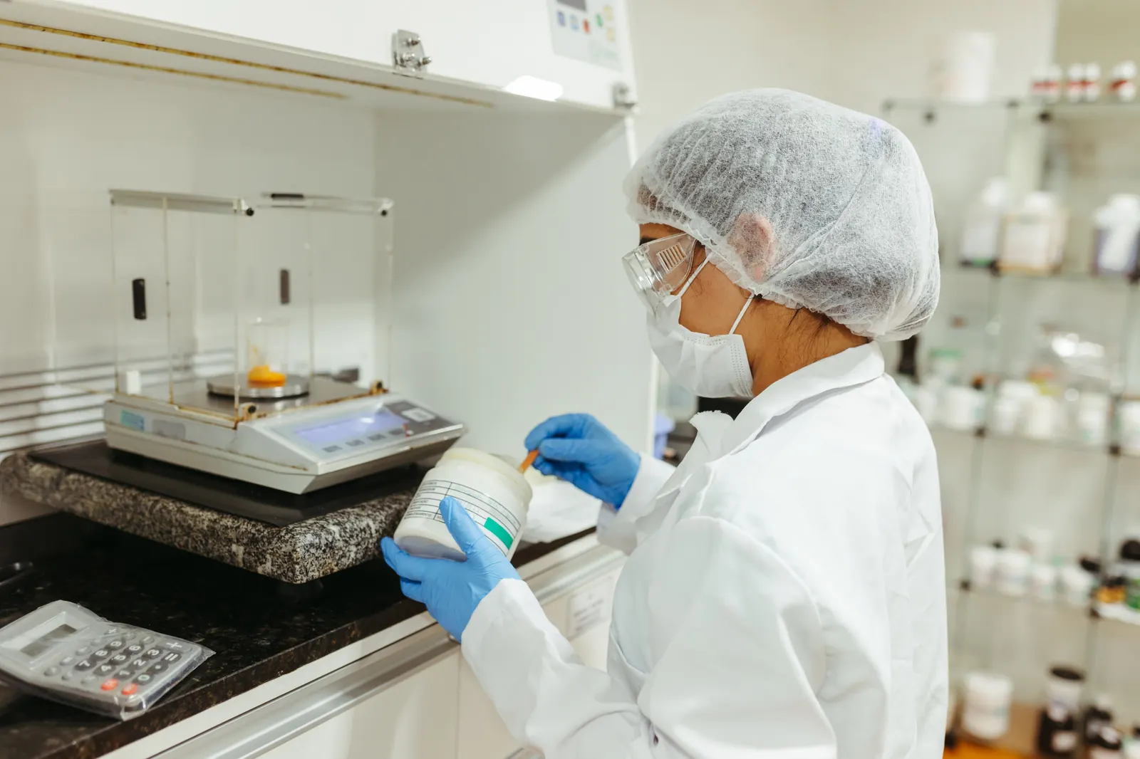 Compounding technician preparing a custom medication at a clean workbench with a precision scale, tools and ingredients